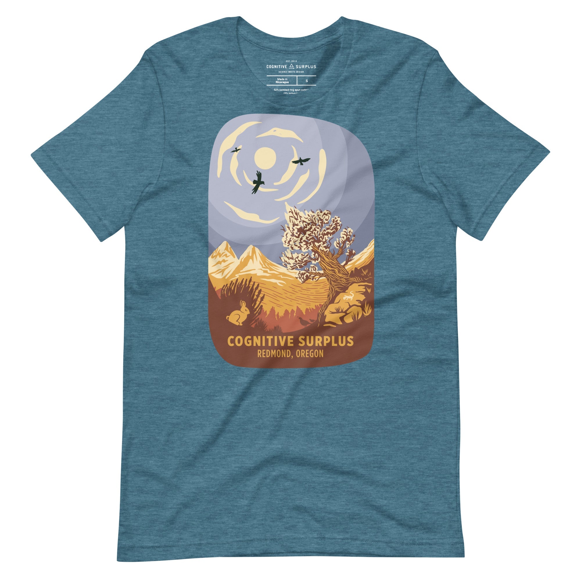 Blue T-shirt featuring an illustration of mountains, trees, birds, and the sun, with the text "Cognitive Surplus, Redmond, Oregon.
