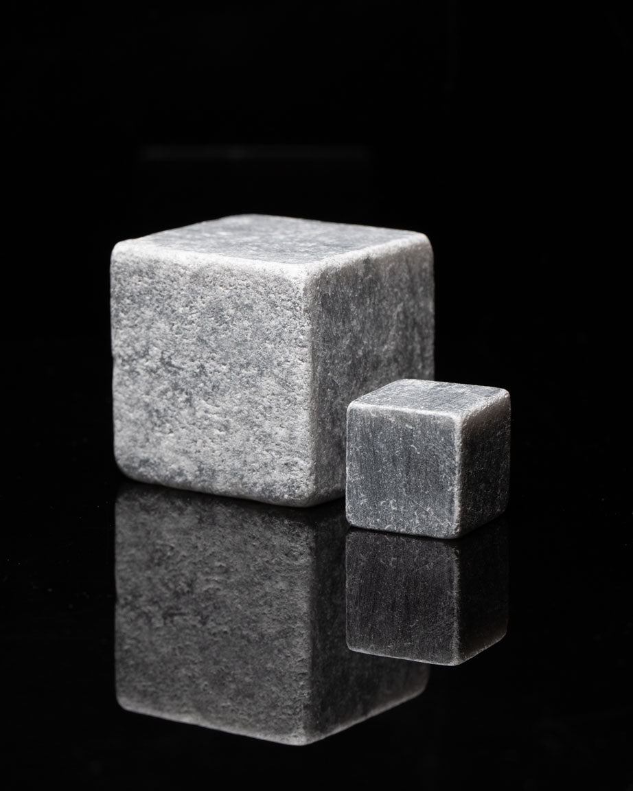 Two Mega Rocks Soapstone Whiskey Stones on a black surface.