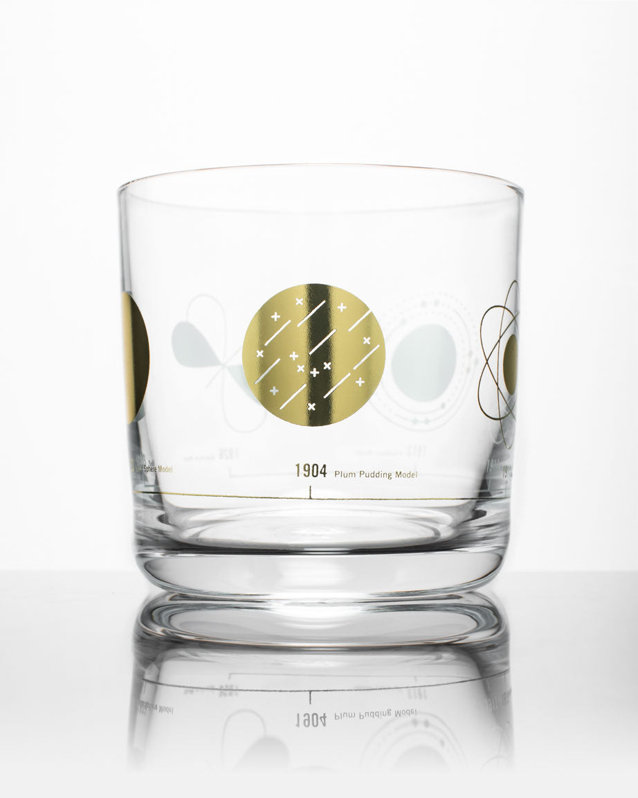 A Cognitive Surplus Atomic Models Whiskey Glass with a gold design on it.